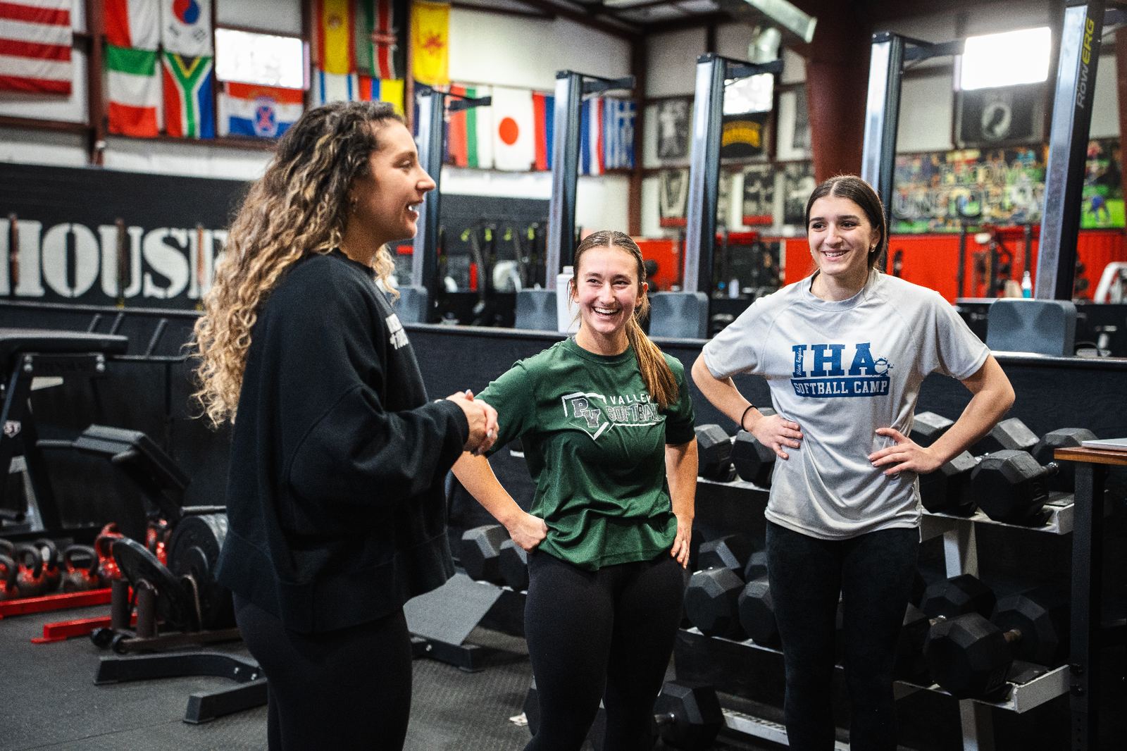 Coach talking with two young athletes beside the dumbbell rack during a training session
