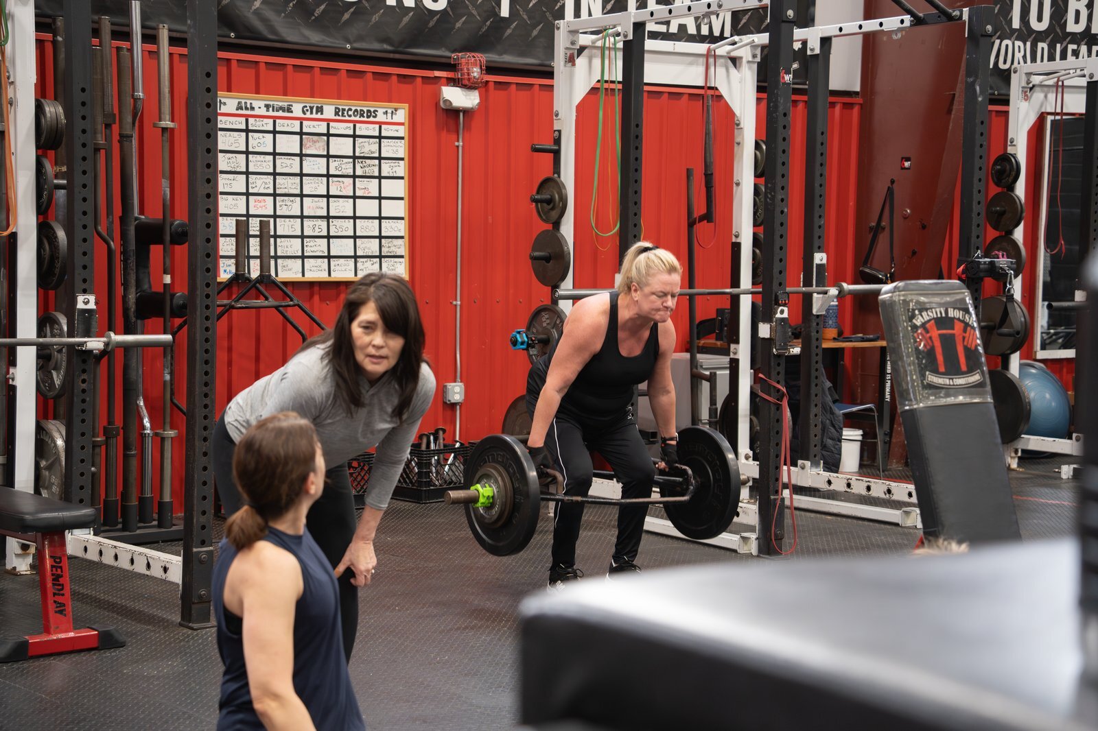Coach guiding a woman through a barbell deadlift at Varsity House