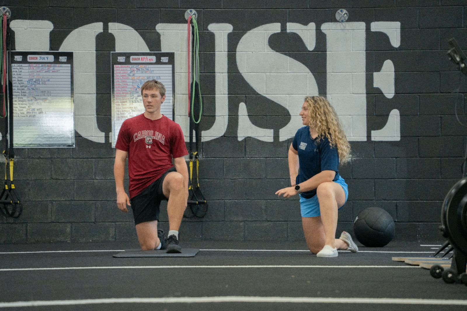 Coach demoing movement quality with a youth athlete in front of the Varsity House wall